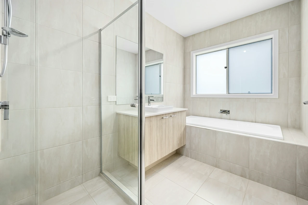 Wide beige tiled bathroom with glass shower, vanity, and bathtub